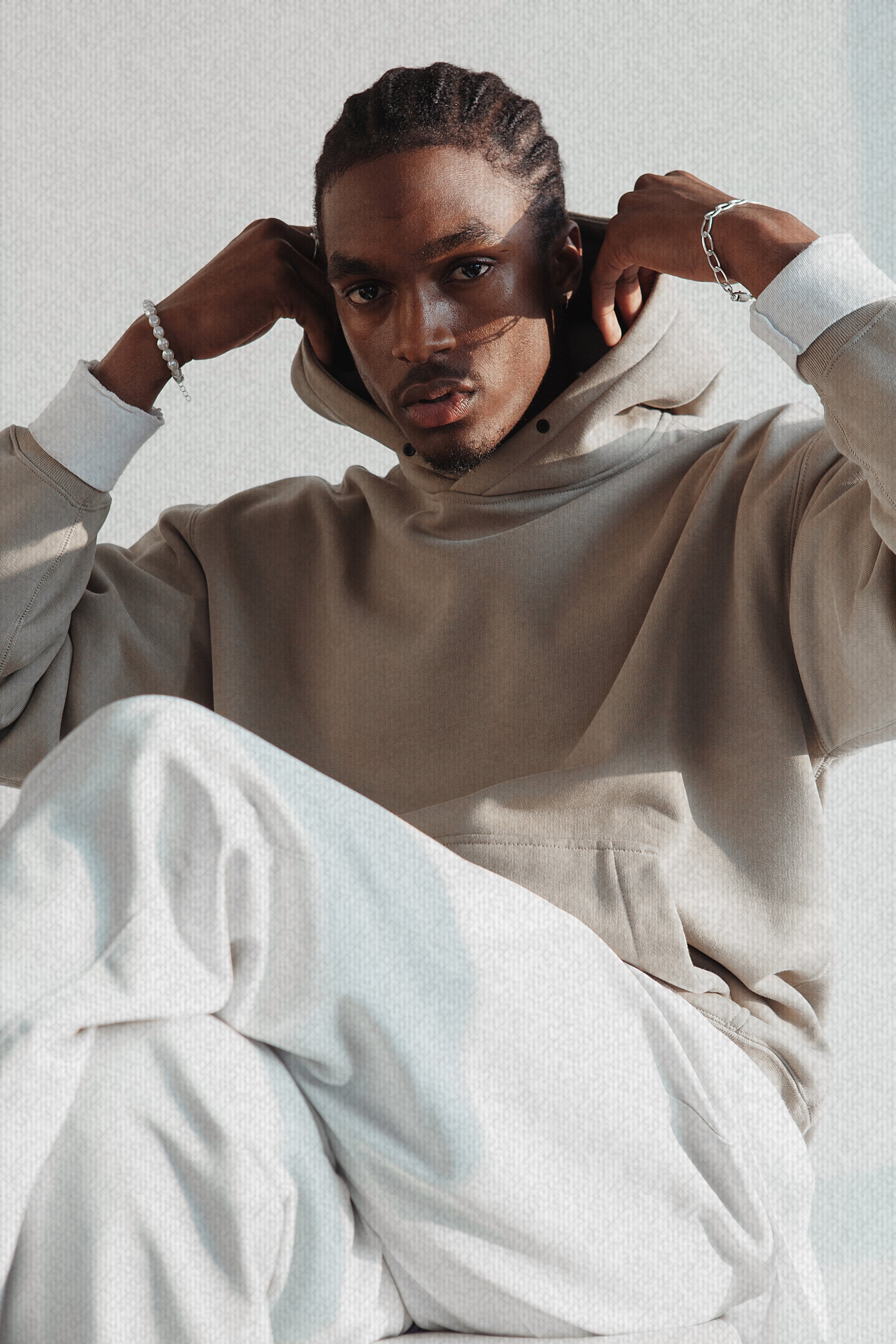 Man wearing a premium beige VIICCE hoodie and white trousers in a minimalist setting. Luxury men's streetwear.
