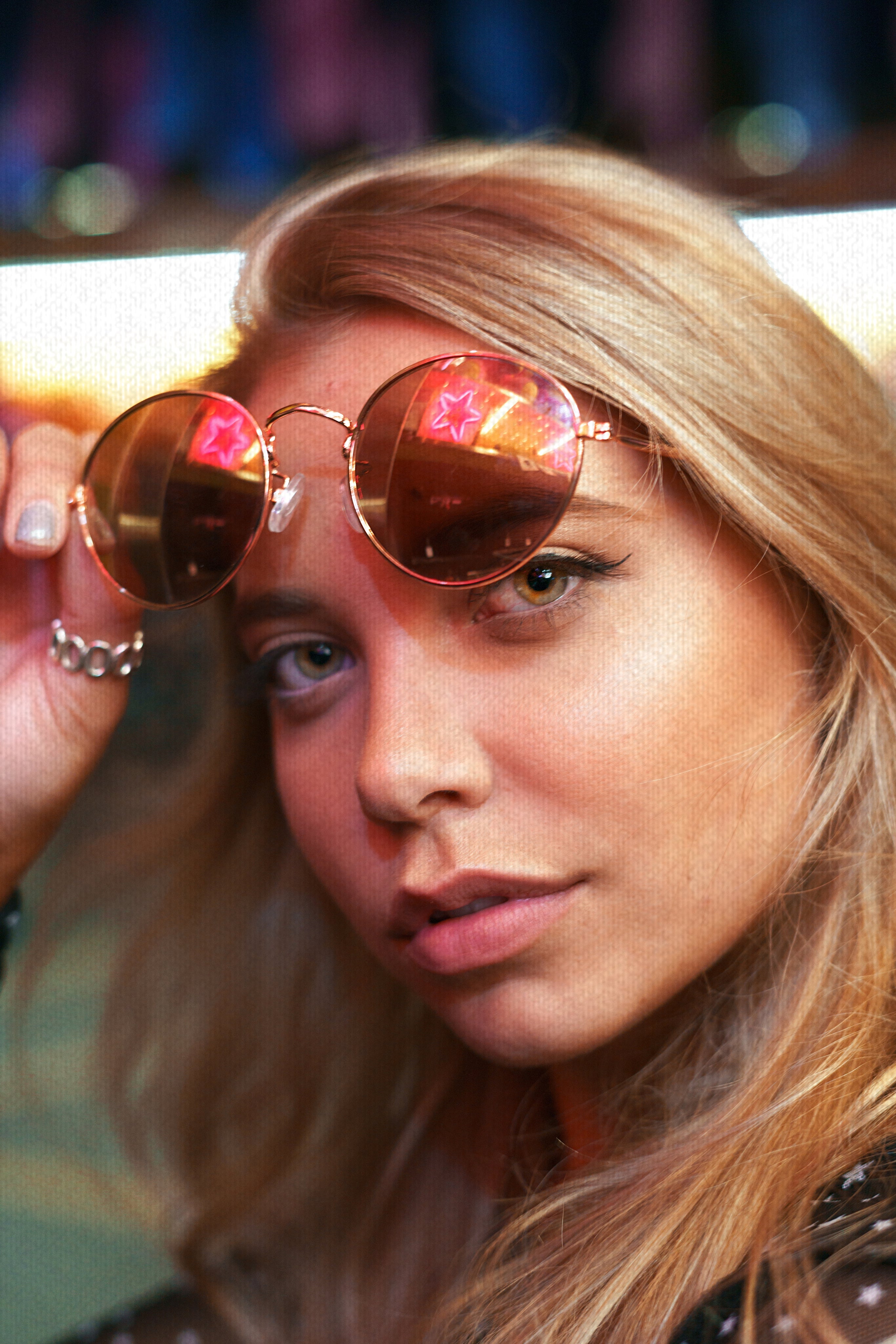 Close-up portrait of a woman wearing VIICCE round sunglasses with red reflective lenses showing a star shape. Urban nightlife fashion.