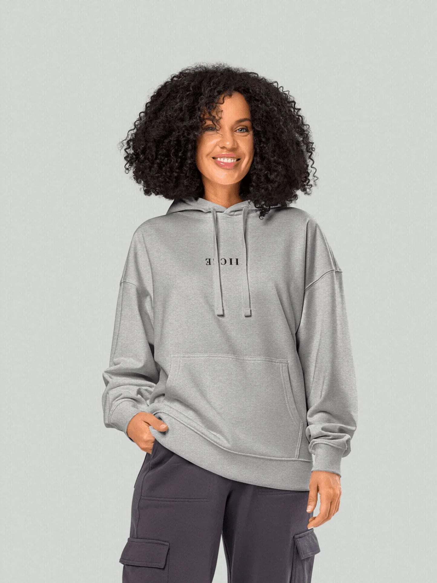 VIICCE Core Heavyweight Hoodie in Concrete Gray. Women's model with Viicce written upside down on the chest. Minimalist streetwear style. Studio photo.