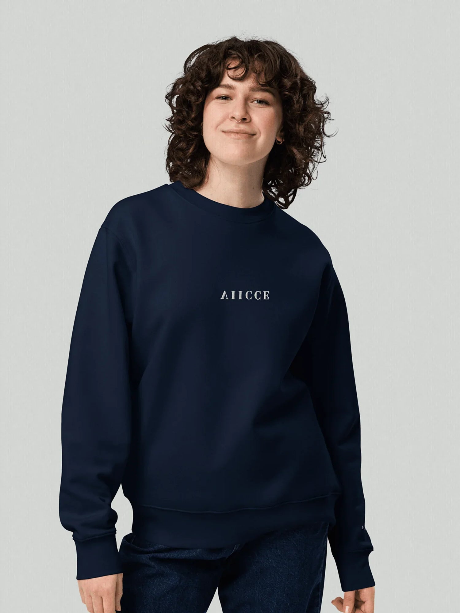 VIICCE Structural Crewneck in Midnight Blue. Female model facing forward wearing a sweatshirt with a loose fit, with "viicce" inverted vertically on the chest and left sleeve. Studio image.